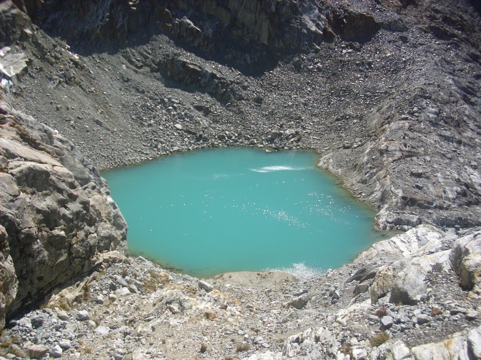 A turquoise lake nestled between rocky mountain slopes with boulders in the foreground