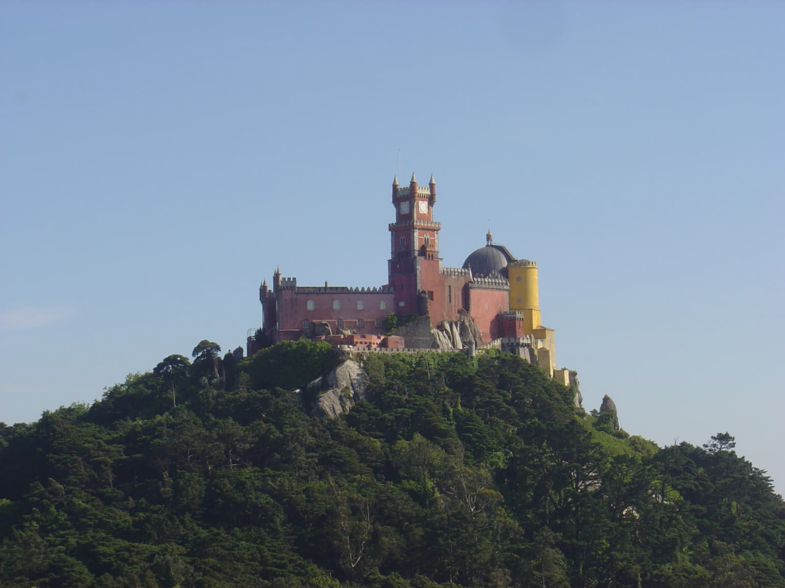 Pena Palace with red and yellow towers on a hilltop surrounded by dense green forest under clear blue sky