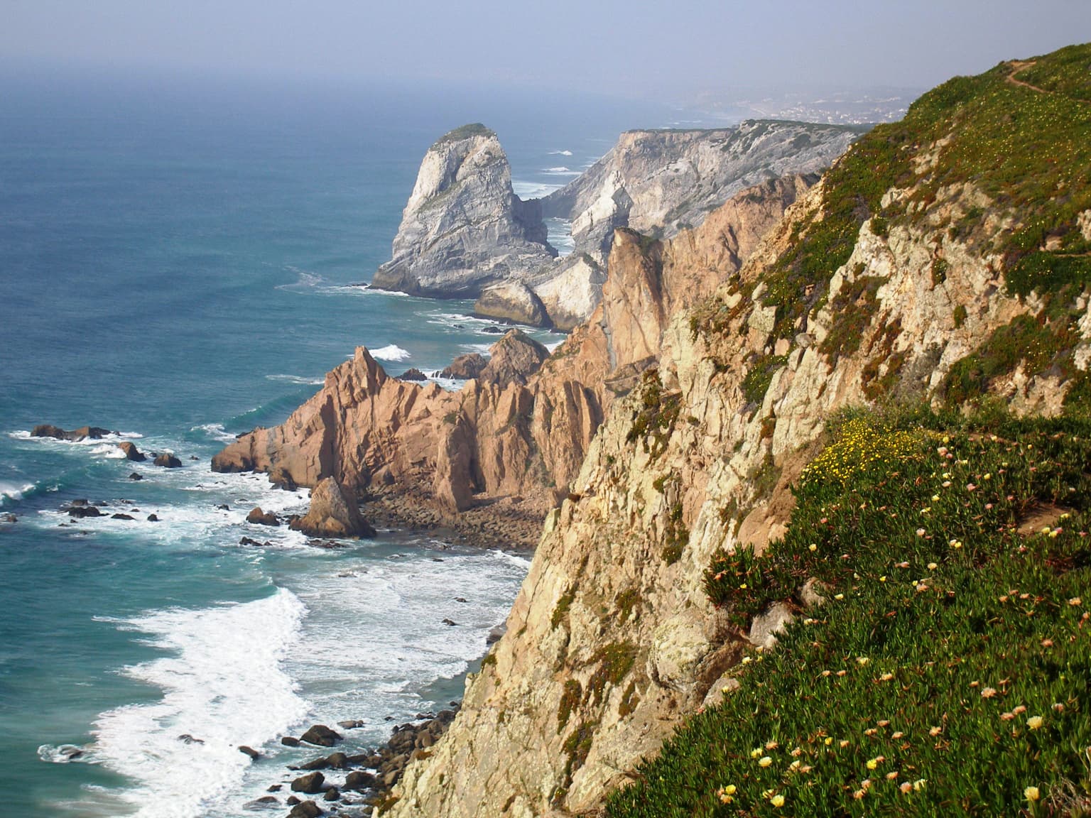 Cliffs along the ocean with waves crashing, green vegetation on the hillside
