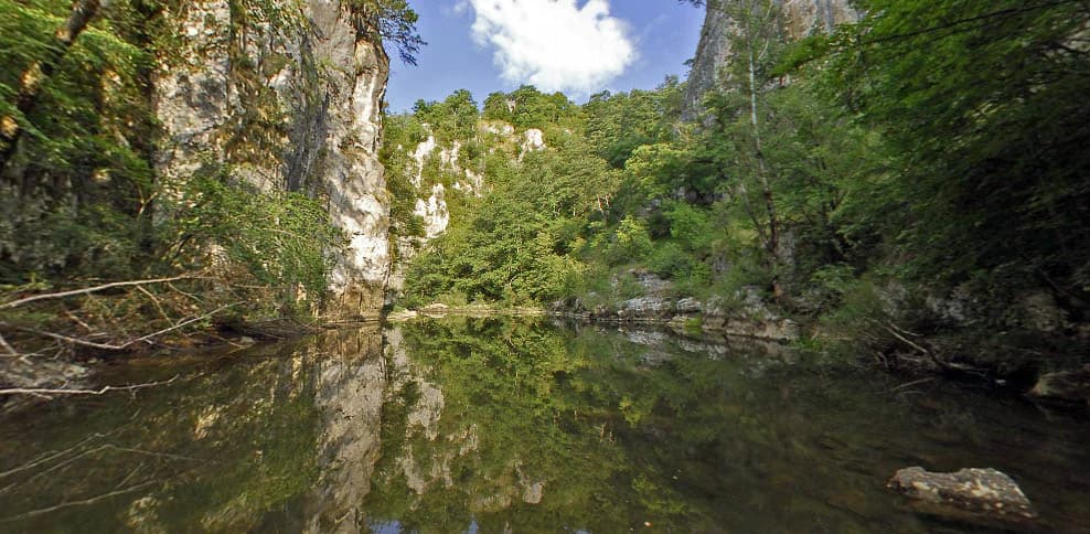 A calm river reflecting steep rocky cliffs and lush green trees in a canyon landscape