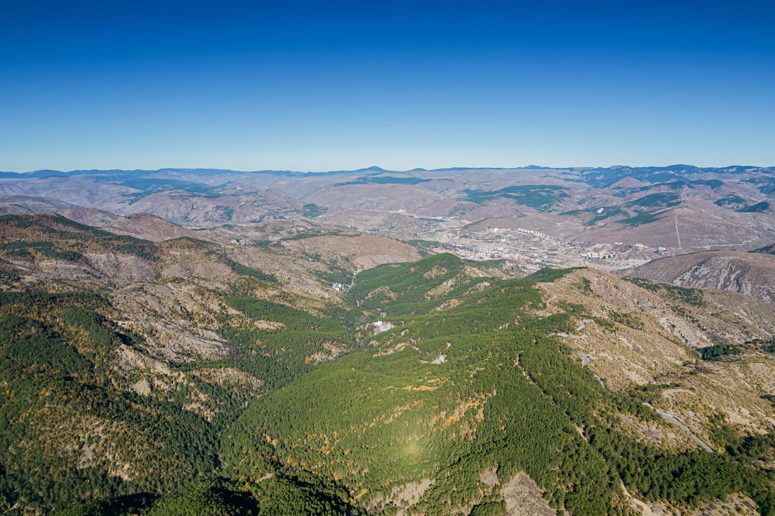 Aerial view of rolling mountains and forested valleys in Soğuksu National Park under a clear blue sky