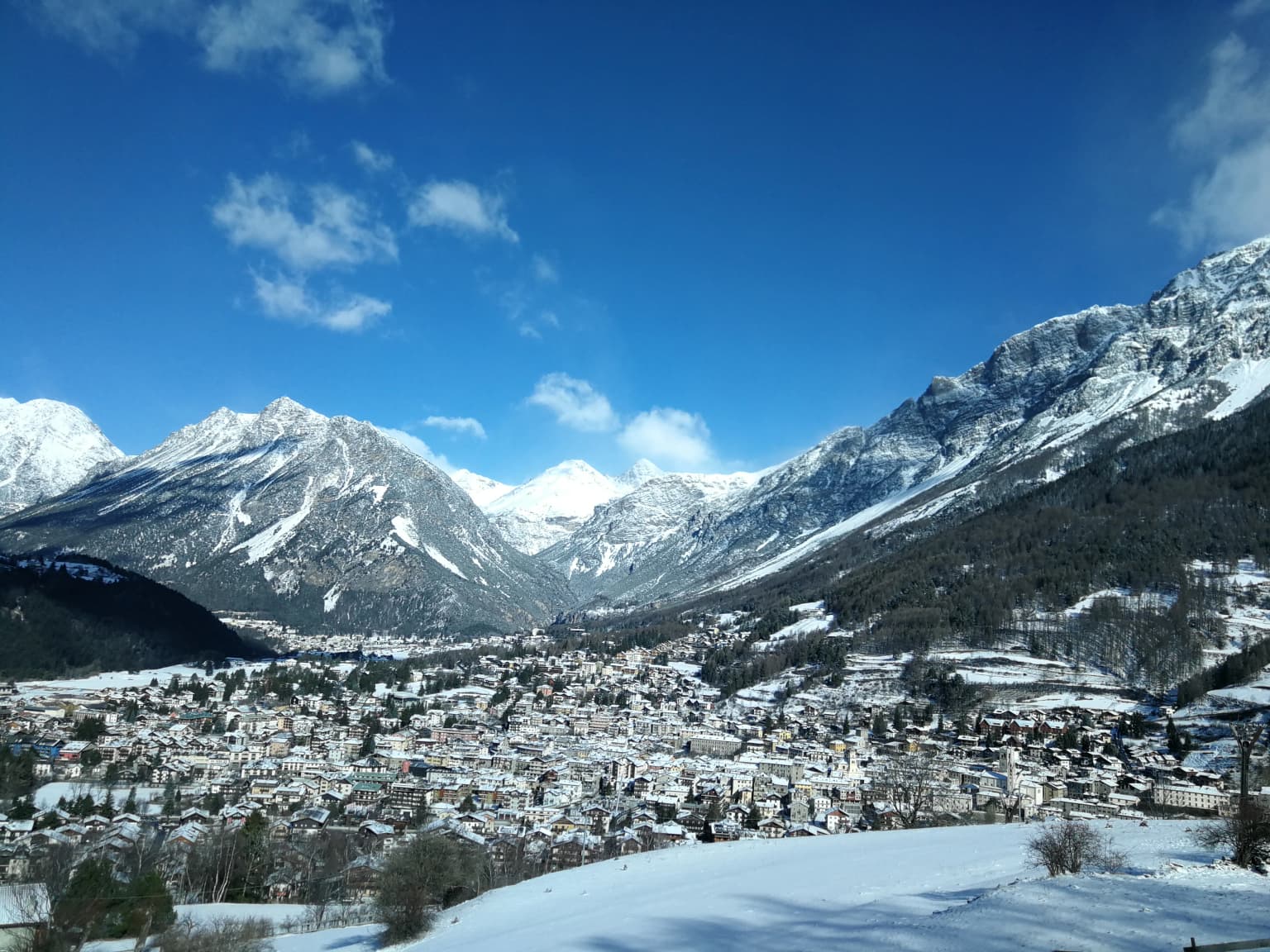 Panoramic view of Bormio town with snow-capped mountains under a clear blue sky