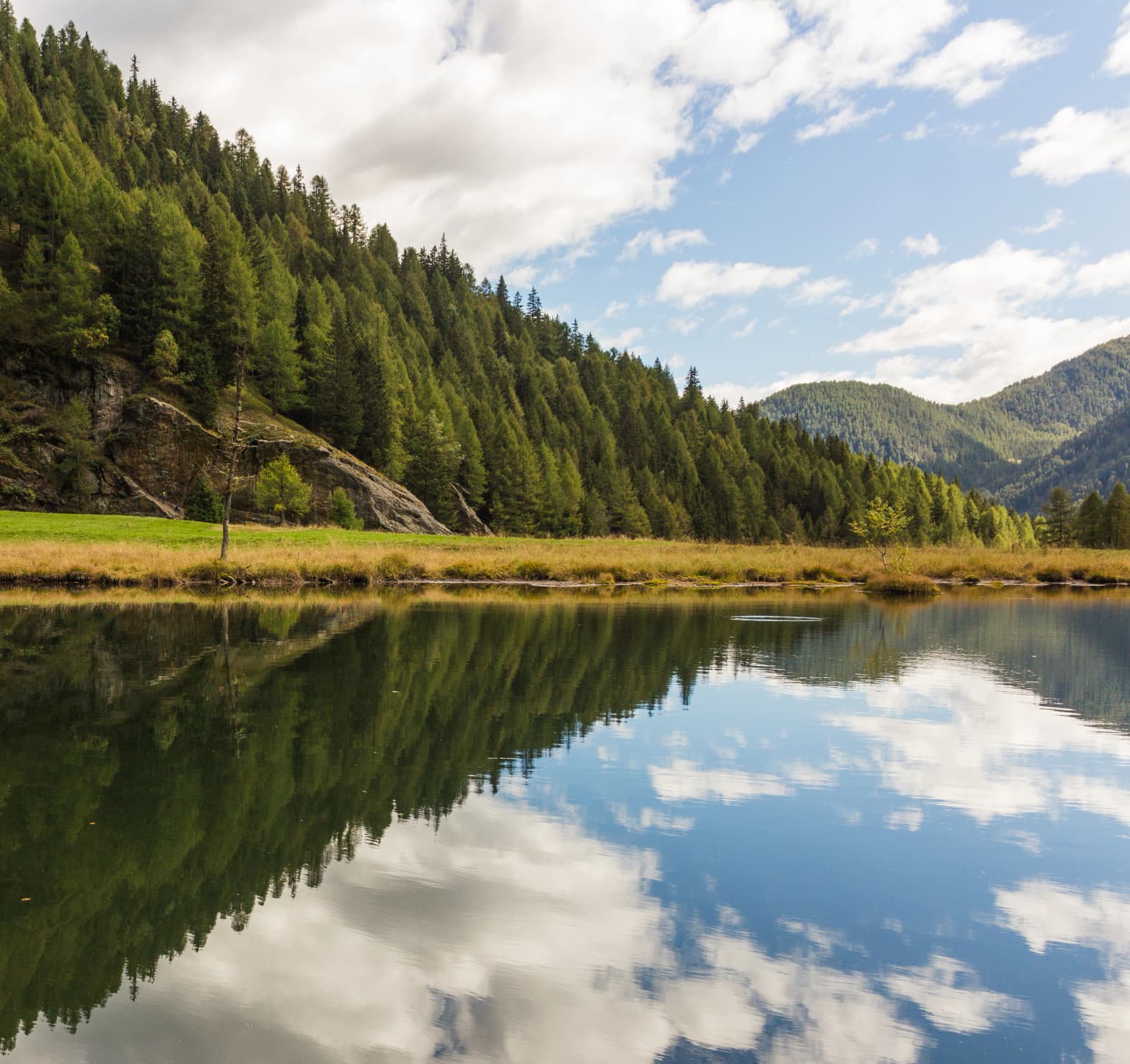 A lake reflecting a forested mountain landscape with clear blue sky and clouds