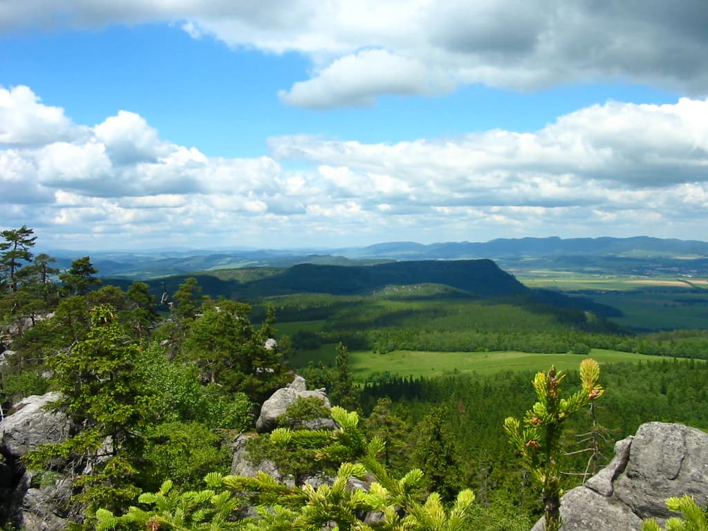 Wide landscape view showing rocky outcrops, dense forests, and a valley under a partly cloudy sky