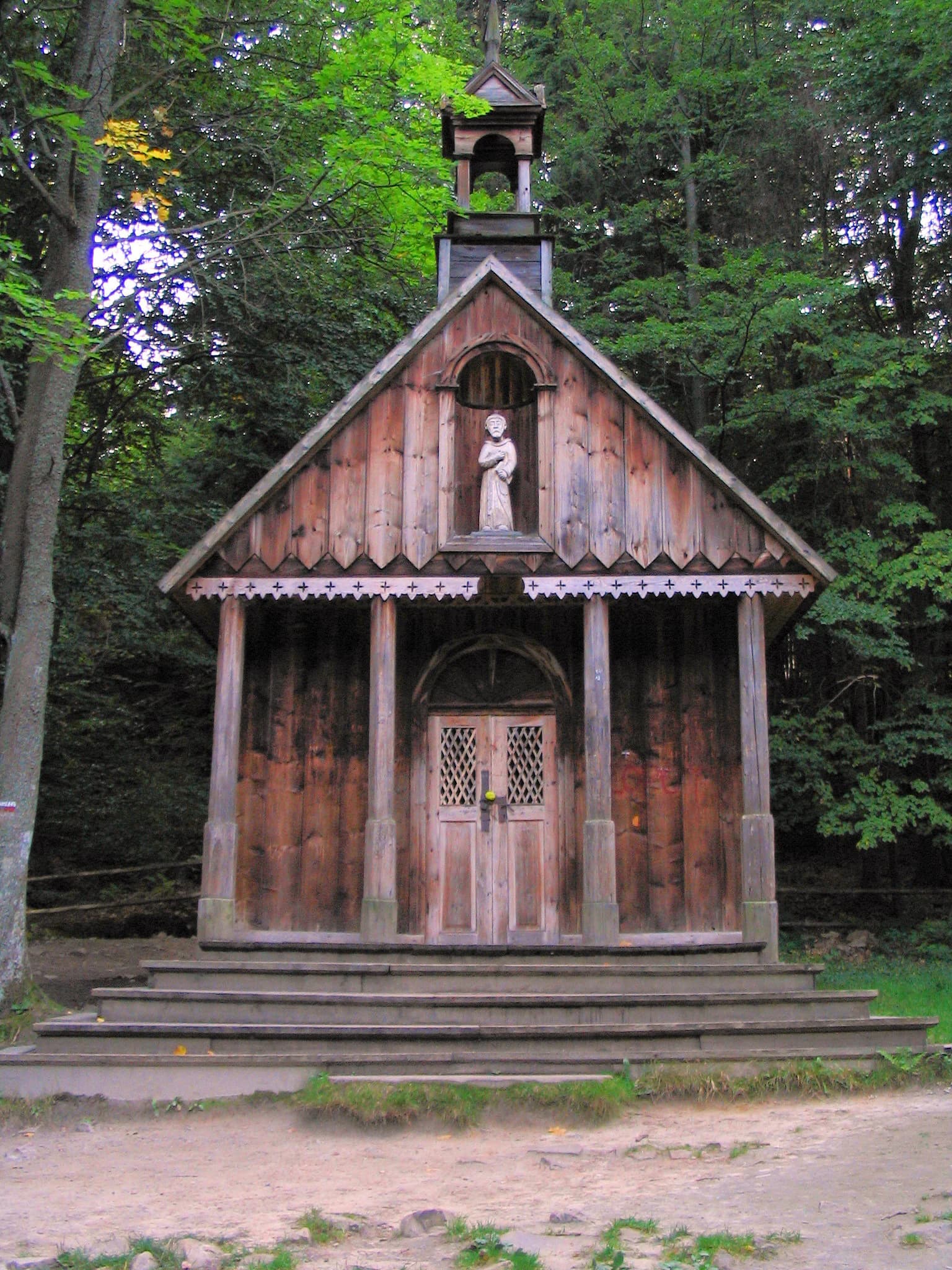 Wooden chapel with statue in gable, surrounded by trees