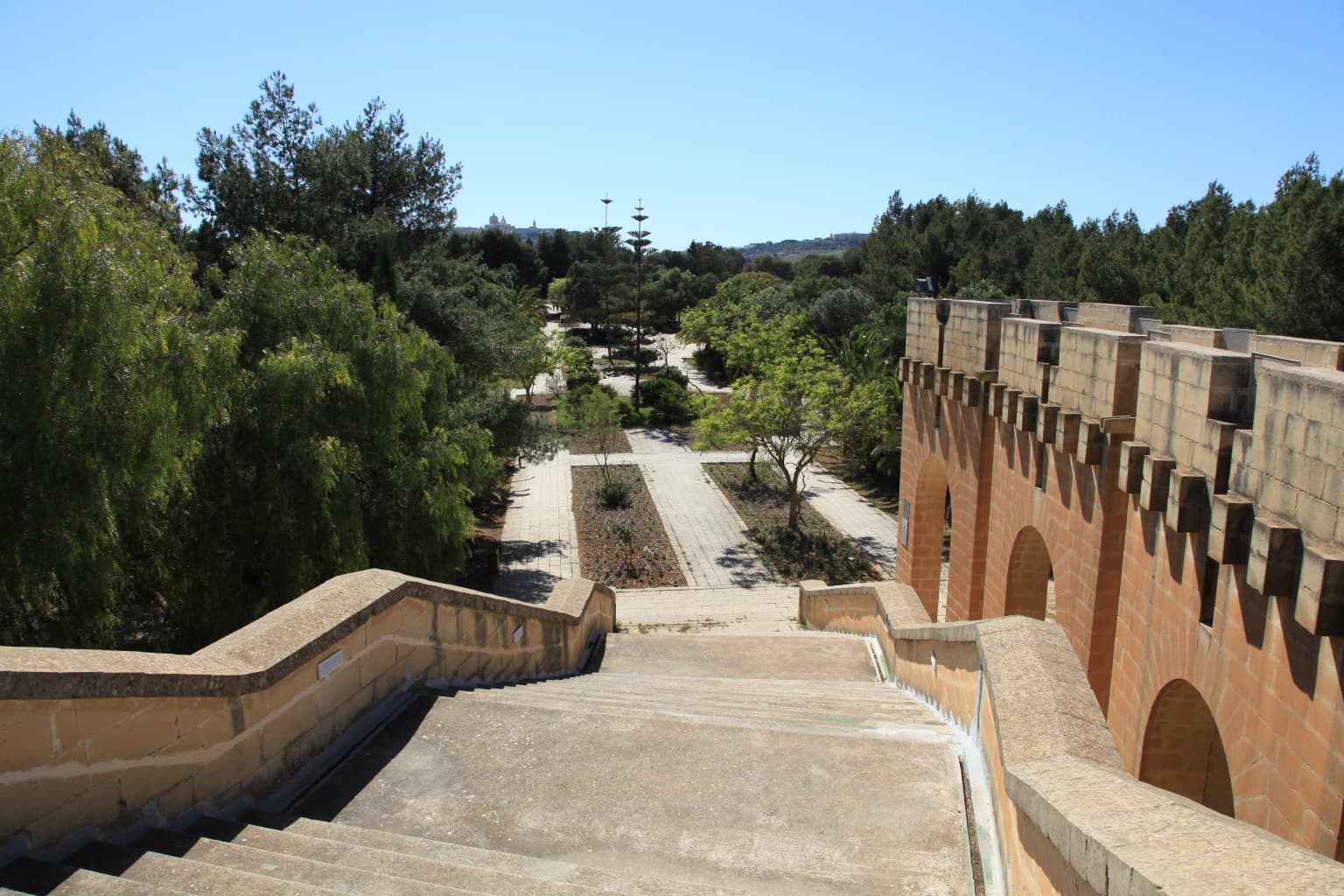 Concrete staircase descending into a park with trees and a historic building featuring arched openings on the right