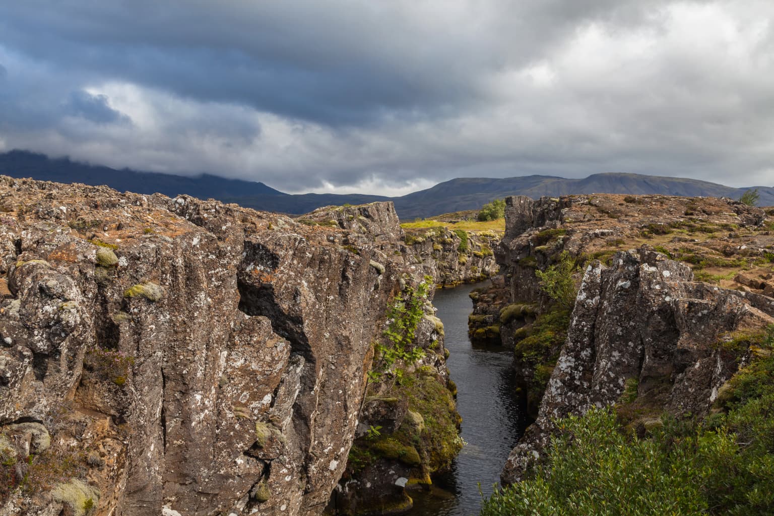 Rugged volcanic rock canyon with a narrow river flowing through, surrounded by steep cliffs under a cloudy sky