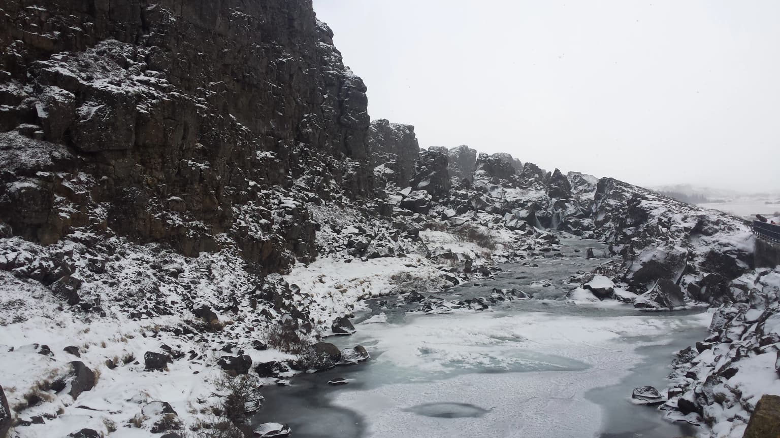 Snow-covered rocky cliffs and frozen river in a valley