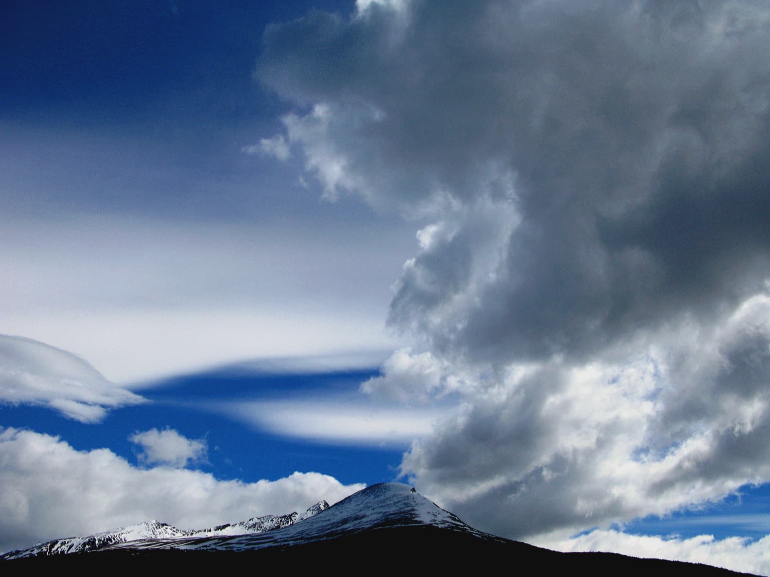 Snow-capped mountain peak under a partly cloudy sky with dark clouds and blue sky