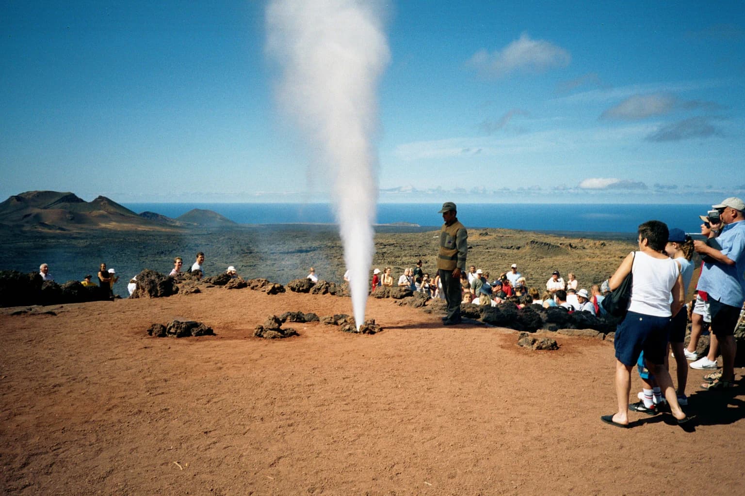 Group of tourists watching steam erupt from the ground in a volcanic landscape with ocean view