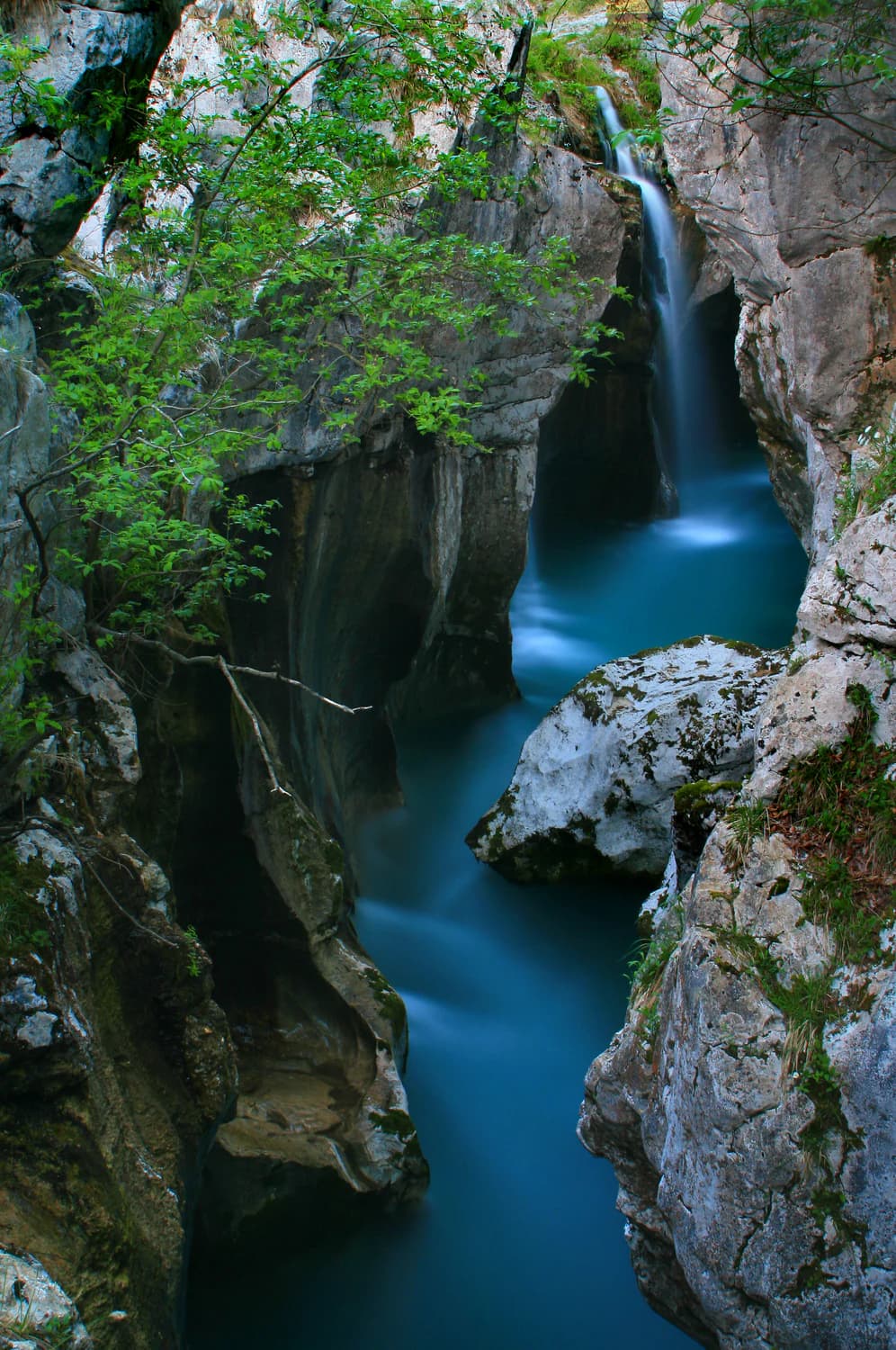 A waterfall cascading through rocky cliffs with a blue river flowing below, surrounded by lush green foliage