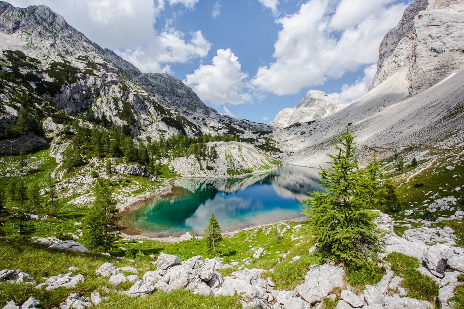 Mountain lake surrounded by rocky slopes and green vegetation under a partly cloudy sky