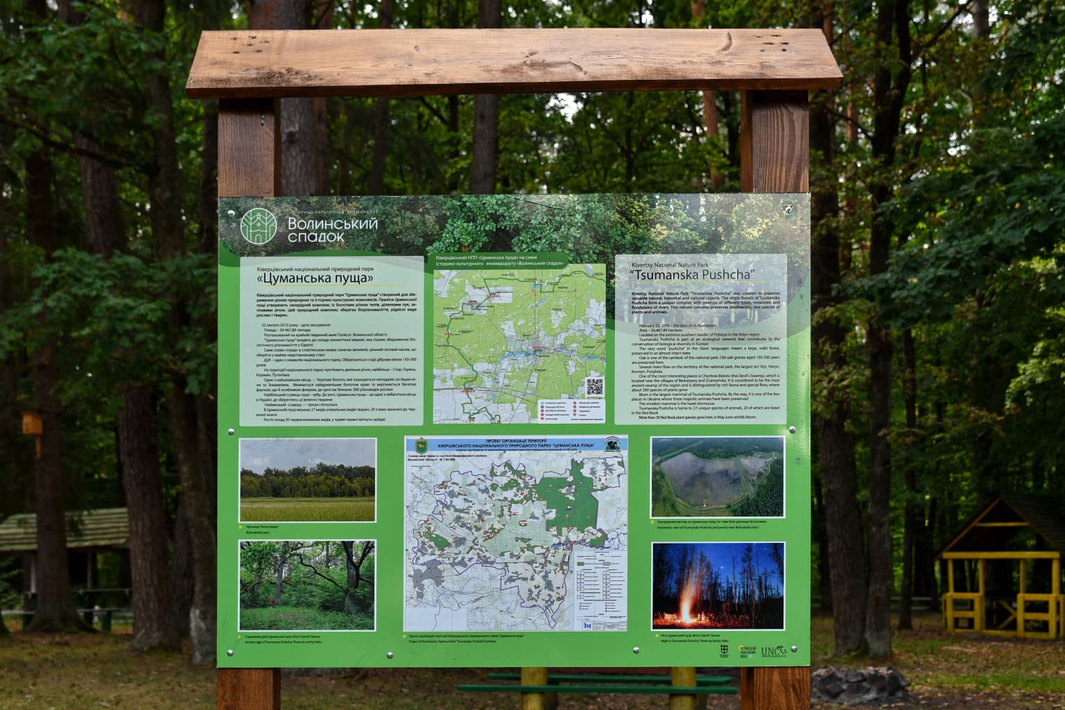 Green information board mounted on wooden posts displaying text, maps, and photographs related to Tsumanska Pushcha National Nature Park