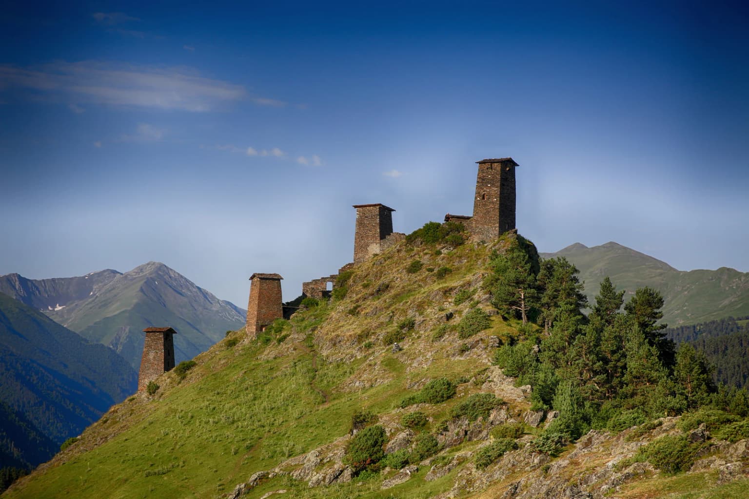 Stone towers on a grassy hilltop with mountains in the background under a clear blue sky