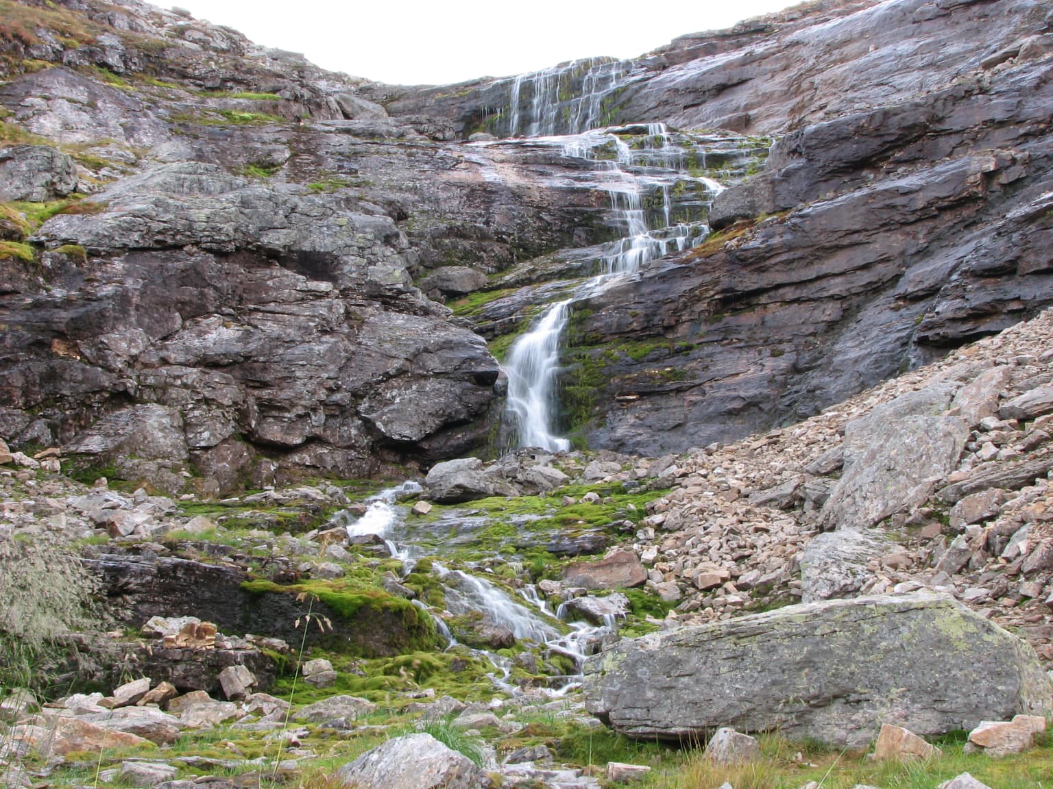 Waterfall cascading down rocky cliffs with moss-covered stones and scattered boulders