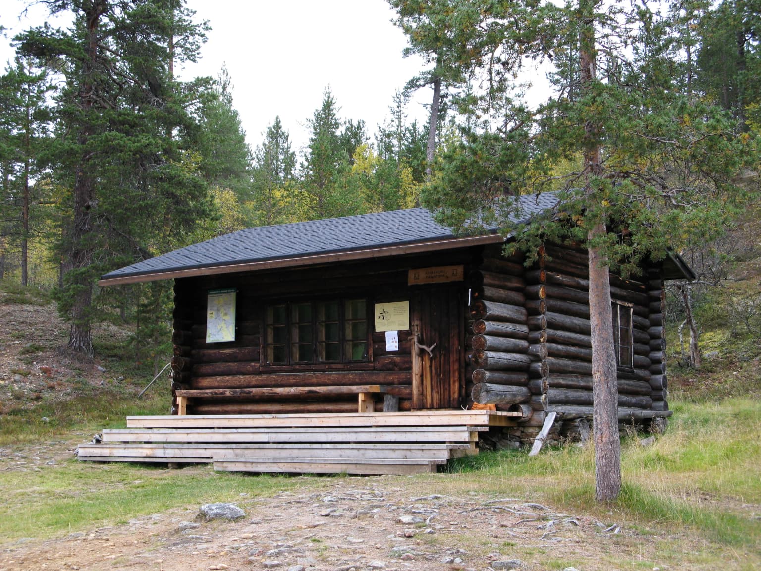 Log cabin structure with wooden steps, surrounded by trees and grass
