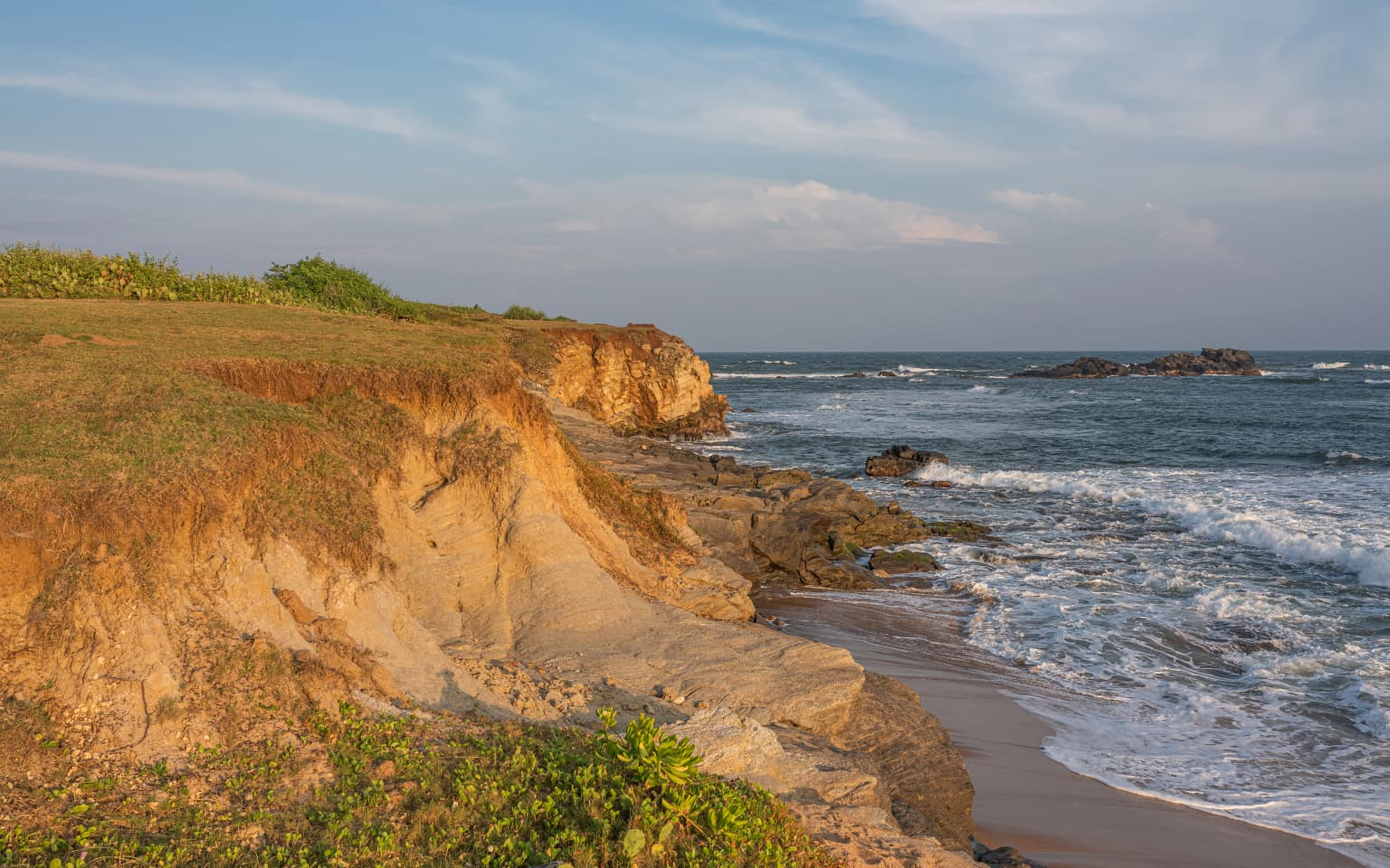 Coastal cliffs with sandy beach and ocean waves under partly cloudy sky