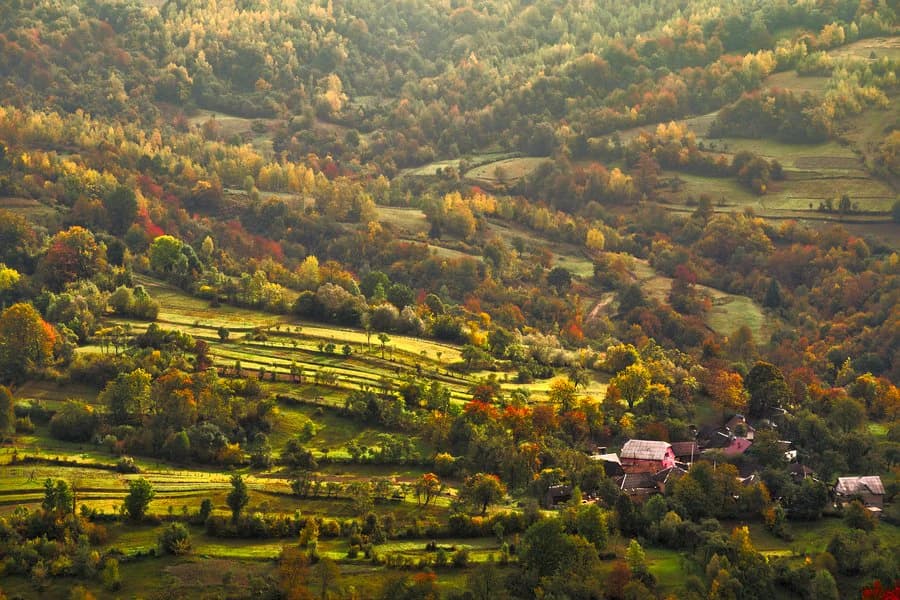 Wide landscape view of hilly terrain with forested areas, agricultural fields, and small houses
