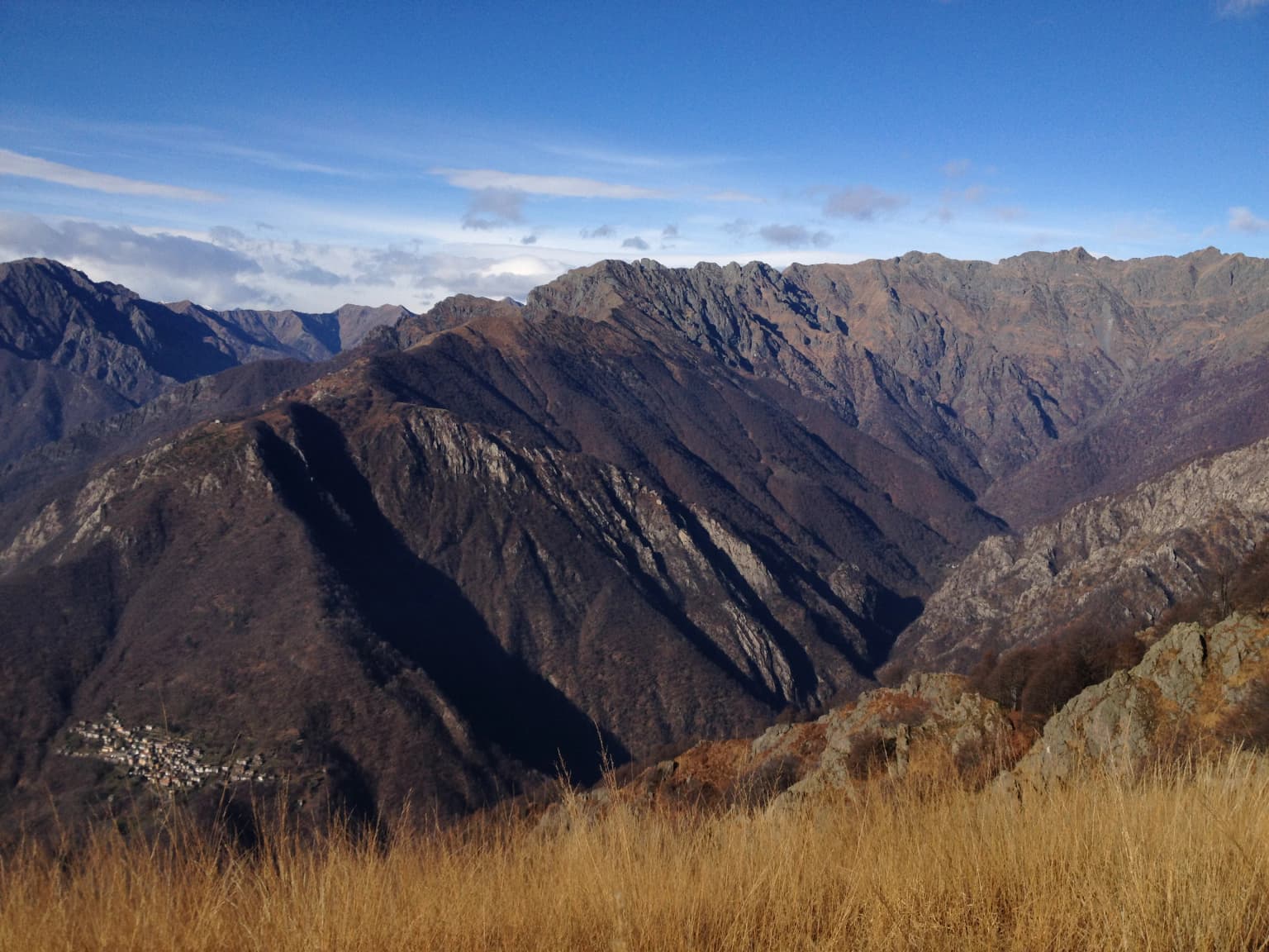 Mountainous landscape with valleys, dry grass in foreground, and clear blue sky