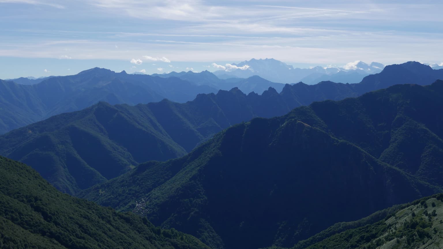 Wide panoramic view of mountain ranges, valleys, and green slopes in Val Grande National Park under a partly cloudy sky