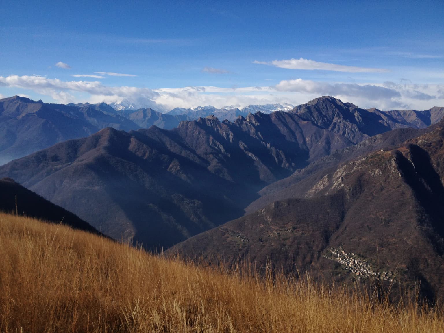 Grassy hillside leading to a valley surrounded by mountain ranges under a clear blue sky