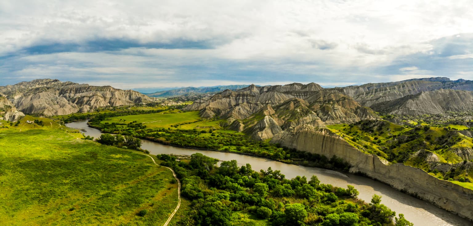 A river winding through grassy hills and rocky badlands under a partly cloudy sky