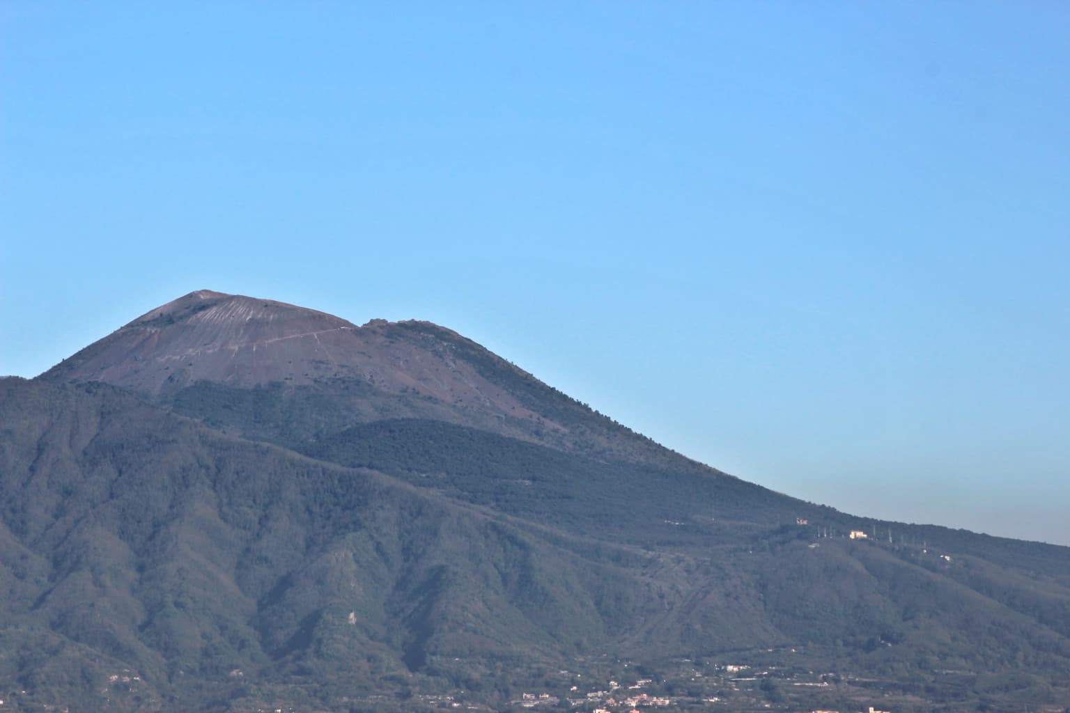 Mount Vesuvius volcano under a clear blue sky with green hills in the foreground