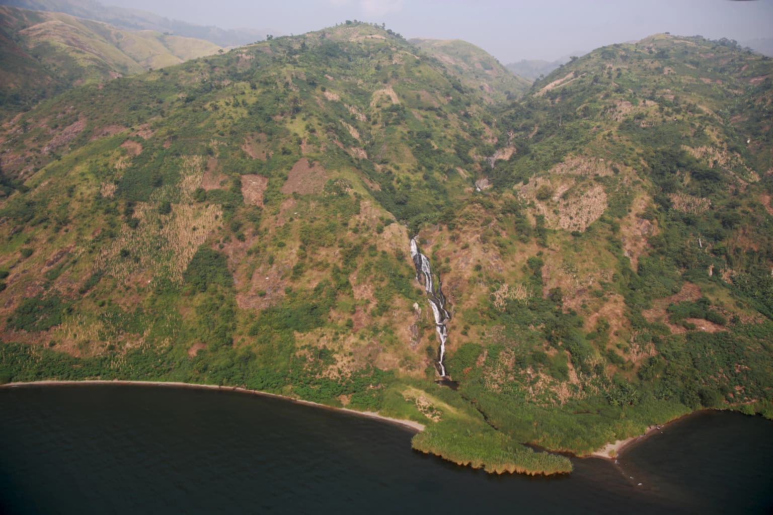 Aerial view of green mountains with a waterfall flowing into a large body of water
