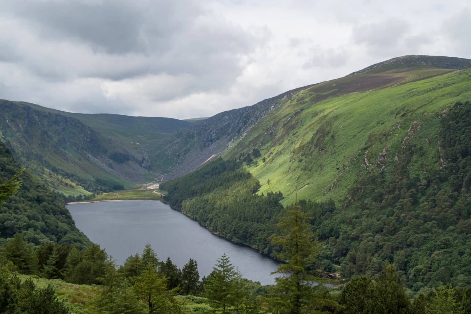 Wide view of Upper Lake surrounded by green hills and forests under a cloudy sky