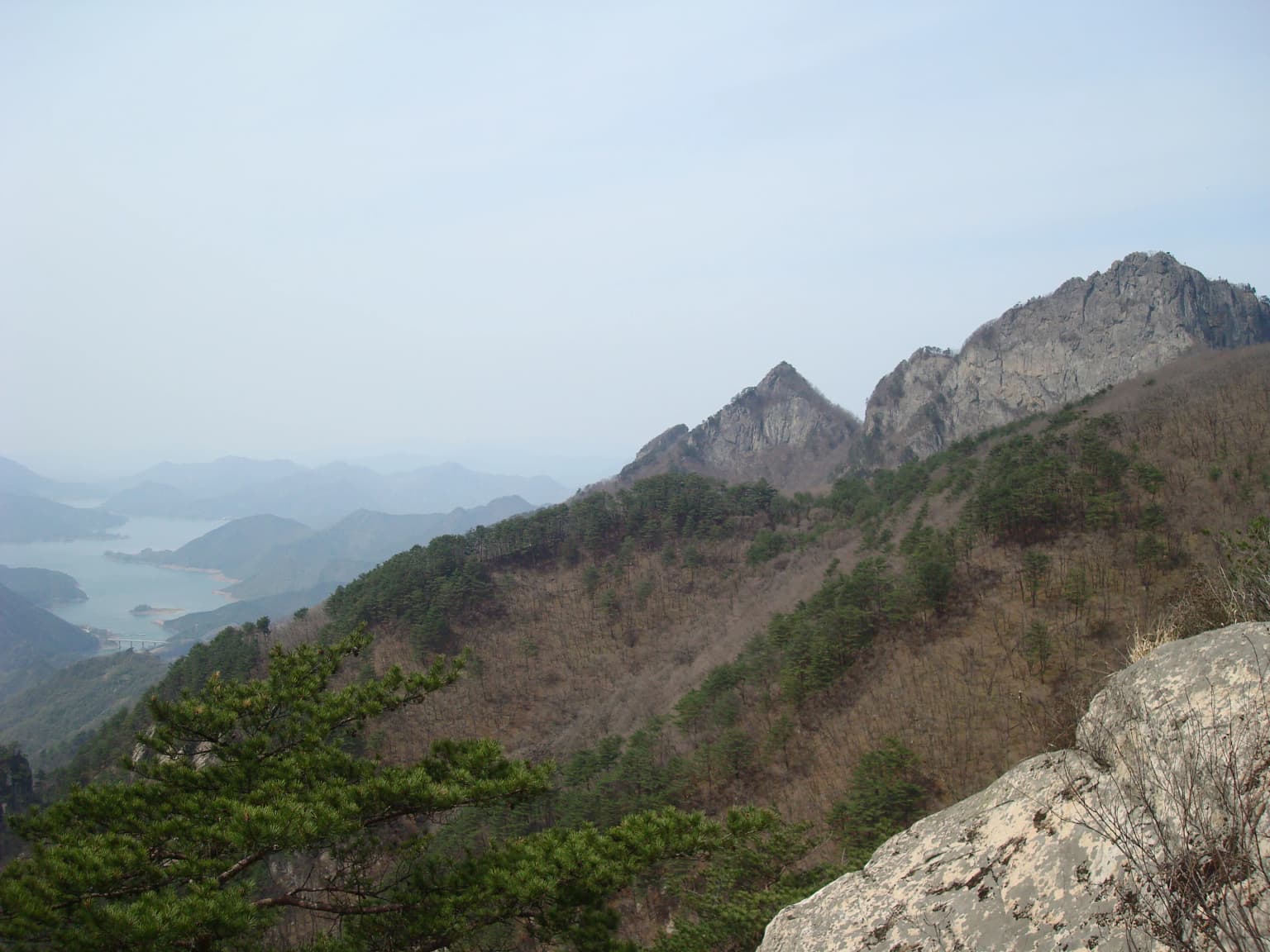 Panoramic view of Mount Worak with rocky peaks, forested slopes, and a body of water in the distance
