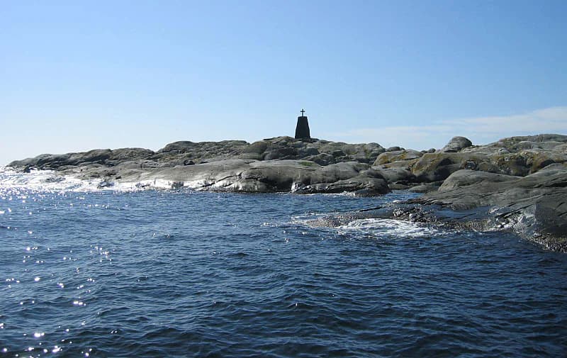 Rocky coastal landscape with water, tower structure on an island, clear blue sky
